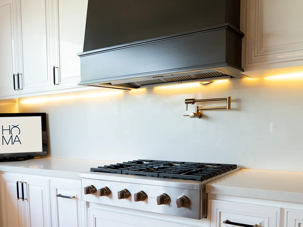 Rangetop de gas Café con perillas en acabado bronce y pot-filler de latón, bajo la campana de chimenea negra