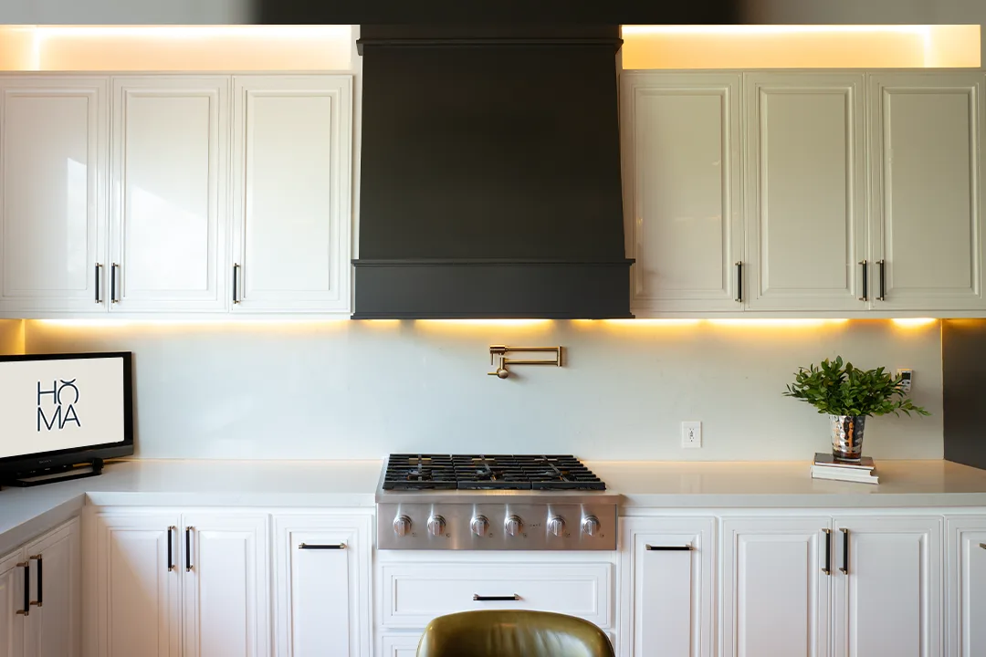 Cocina de gabinetes blancos con campana de chimenea negra, rangetop Café y pantalla con el logo de Homa