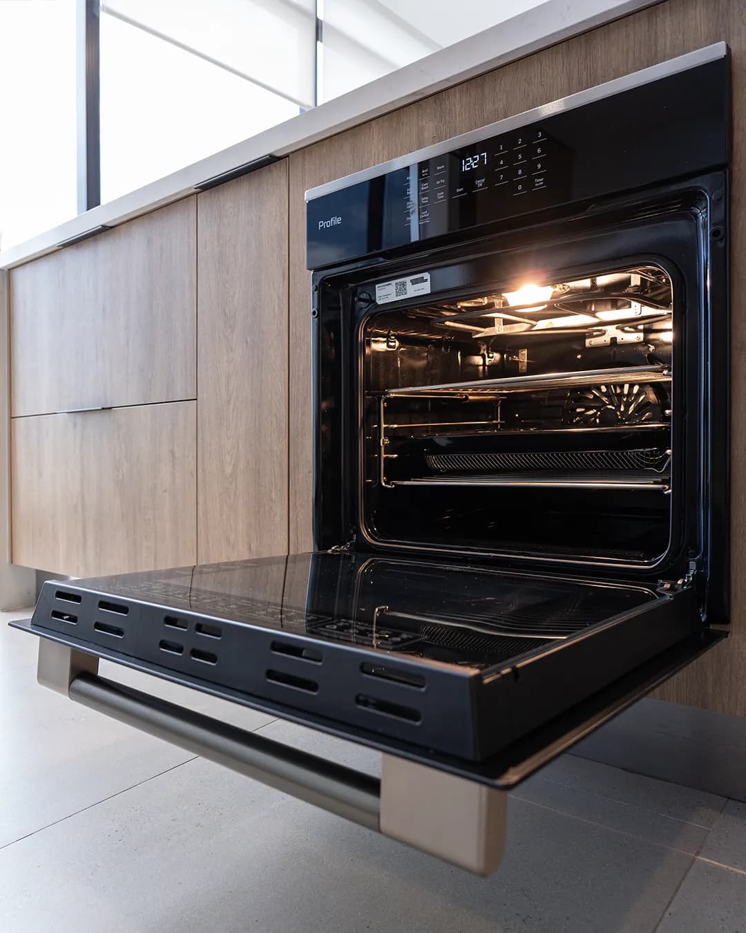 Horno GE Profile abierto e iluminado, empotrado en gabinetes de madera clara